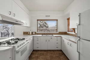 Kitchen featuring sink, white appliances, white cabinetry, and backsplash