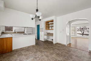 Kitchen with white refrigerator, a notable chandelier, sink, tasteful backsplash, and pendant lighting