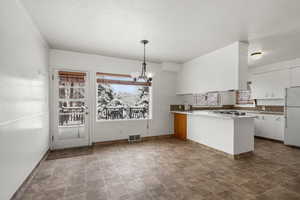 Kitchen featuring kitchen peninsula, white refrigerator, a healthy amount of sunlight, white cabinets, and pendant lighting