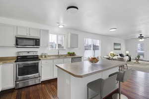 Kitchen featuring stainless steel appliances, a kitchen island, a sink, open floor plan, and dark wood-style floors