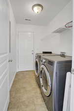 Washroom featuring washing machine and dryer, laundry area, visible vents, and baseboards