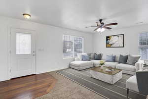 Living room with ceiling fan, dark wood-type flooring, visible vents, and baseboards