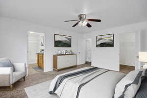 Bedroom featuring light carpet, baseboards, a ceiling fan, ensuite bathroom, and a walk in closet