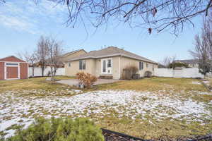 Snow covered property featuring an outbuilding, a fenced backyard, stucco siding, a storage unit, and a patio area