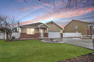 View of front of home featuring brick siding, a front yard, fence, a garage, and driveway