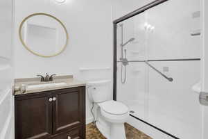 Full bathroom with toilet, a stall shower, stone finish flooring, and vanity