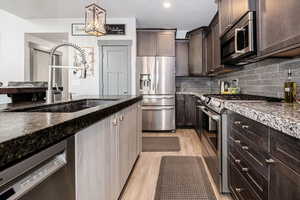 Kitchen featuring dark brown cabinets, stainless steel appliances, a sink, decorative backsplash, and dark stone counters