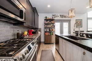 Kitchen with light wood-style flooring, dark brown cabinets, a sink, decorative light fixtures, and appliances with stainless steel finishes