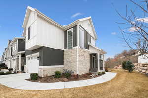 View of home's exterior featuring stone siding, a yard, board and batten siding, driveway, and an attached garage