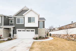 View of front of property featuring concrete driveway, stone siding, a garage, and fence