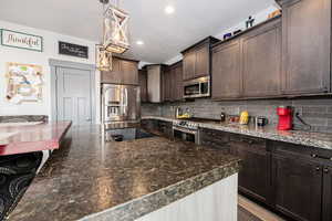 Kitchen featuring dark brown cabinetry, decorative light fixtures, appliances with stainless steel finishes, and decorative backsplash