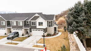 View of front of home with fence, driveway, stone siding, roof with shingles, and a mountain view