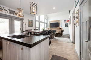 Kitchen with open floor plan, an island with sink, a sink, decorative light fixtures, and dark countertops