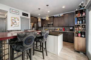 Kitchen with dark brown cabinets, a kitchen island with sink, appliances with stainless steel finishes, pendant lighting, and a kitchen bar