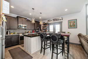 Kitchen featuring tasteful backsplash, pendant lighting, a kitchen bar, a kitchen island with sink, and appliances with stainless steel finishes