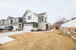 View of side of property with concrete driveway, stone siding, a yard, board and batten siding, and fence