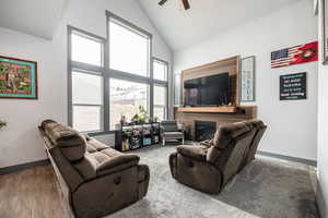 Living area featuring wood finished floors, a ceiling fan, baseboards, high vaulted ceiling, and a glass covered fireplace