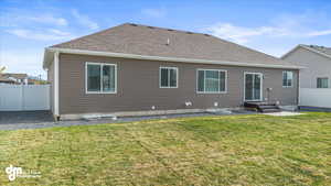 Rear view of house featuring roof with shingles, fence, and a yard