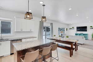 Kitchen featuring white cabinets, open floor plan, hanging light fixtures, stainless steel dishwasher, and a center island