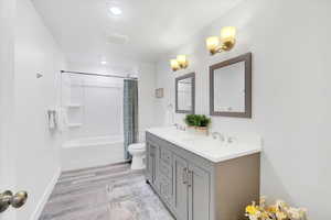 Bathroom featuring double vanity, shower / bath combo, toilet, wood finished floors, and a sink