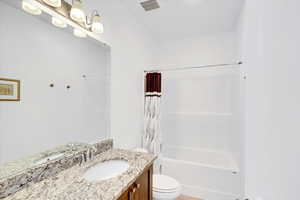 Bathroom featuring toilet, shower / tub combo, vanity, and visible vents