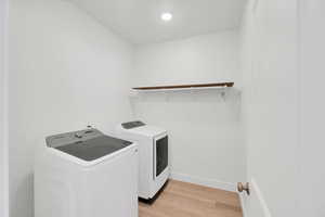 Laundry area featuring laundry area, light wood-style flooring, baseboards, and washing machine and clothes dryer