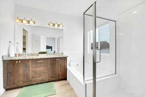 Full bath with double vanity, a sink, a shower stall, wood finished floors, and a bath