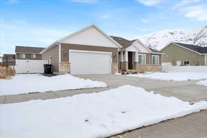 View of front facade featuring an attached garage, stone siding, fence, and a mountain view