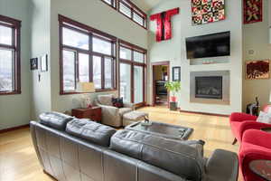 Living room with a glass covered fireplace, plenty of natural light, light wood-style flooring, and a towering ceiling