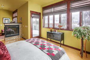 Bedroom featuring baseboards, access to exterior, light wood-type flooring, a tiled fireplace, and a wood stove