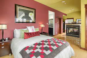 Bedroom with lofted ceiling, recessed lighting, a multi sided fireplace, baseboards, and light wood-type flooring