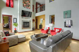 Living area with baseboards, a glass covered fireplace, a towering ceiling, and light wood-style floors