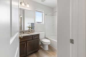 Bathroom with washtub / shower combination, vanity, toilet, and wood finished floors