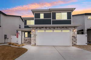 View of front facade featuring a garage, stone siding, driveway, and fence