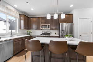 Kitchen with hanging light fixtures, a kitchen island, appliances with stainless steel finishes, and light countertops