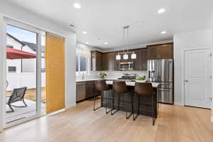 Kitchen featuring light wood-style flooring, appliances with stainless steel finishes, a center island, light countertops, and pendant lighting