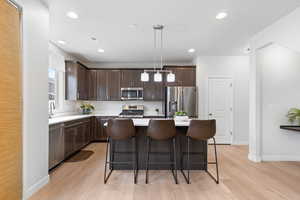 Kitchen with light countertops, hanging light fixtures, light wood-style flooring, appliances with stainless steel finishes, and a kitchen island