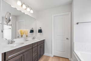 Full bath featuring double vanity, wood finished floors, tiled tub, and a sink