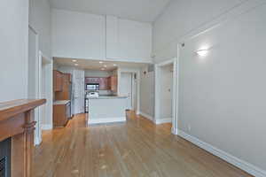 Kitchen with brown cabinets, light wood finished floors, stainless steel appliances, visible vents, and a high ceiling