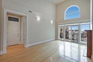 Unfurnished room with light wood-style floors, baseboards, visible vents, and a high ceiling