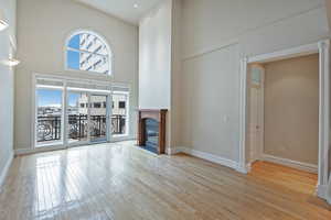 Unfurnished living room featuring a towering ceiling, light wood finished floors, baseboards, and a glass covered fireplace