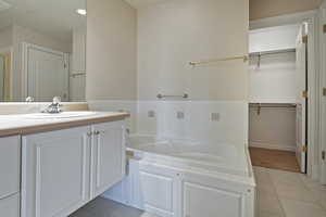 Full bath with a spacious closet, a garden tub, vanity, and tile patterned floors