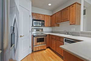 Kitchen featuring light wood finished floors, brown cabinetry, stainless steel appliances, light countertops, and a sink