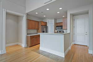 Kitchen with brown cabinets, stainless steel appliances, light countertops, light wood-type flooring, and baseboards