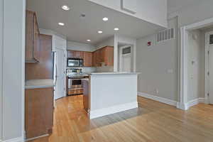 Kitchen featuring stainless steel appliances, light countertops, brown cabinets, and visible vents