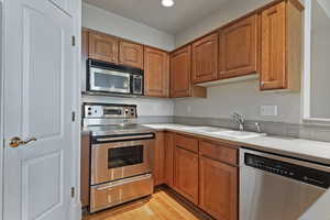 Kitchen featuring stainless steel appliances, brown cabinets, light countertops, and a sink