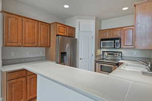 Kitchen featuring light countertops, appliances with stainless steel finishes, brown cabinetry, and a sink