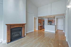 Unfurnished living room featuring light wood-type flooring, a towering ceiling, baseboards, and a fireplace