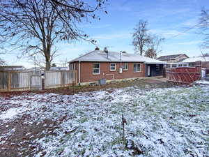 Snow covered rear of property featuring brick siding, a patio, central air condition unit, a gate, and fence