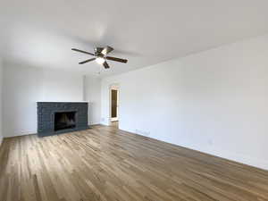 Unfurnished living room with visible vents, baseboards, a ceiling fan, a fireplace with flush hearth, and light wood-style floors